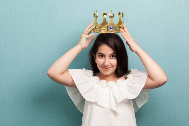 young beautiful princess brunette girl in white dress wearing golden diadem crown and looking at camera on blue background - Φωτογραφία, εικόνα