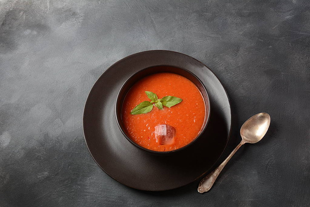 Томатный гаспачо суп с перцем и чесноком, базилик. Испанская кухня. Томатный холодный суп в черной миске на темном фоне
 - Фото, изображение