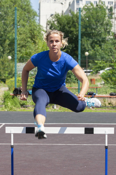 A beautiful and athletic girl is running hurdles in the stadium - Valokuva, kuva