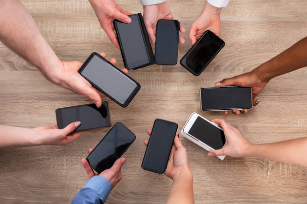 Top View Of People's Hand Showing Blank Display Mobile Phone Above Wooden Backdrop - Foto, Imagem