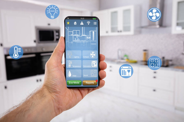 Nahaufnahme der Hand des Menschen, die ein Mobiltelefon hält, mit Smart Home Control-Icon-Funktion mit Küchenhintergrund - Foto, Bild