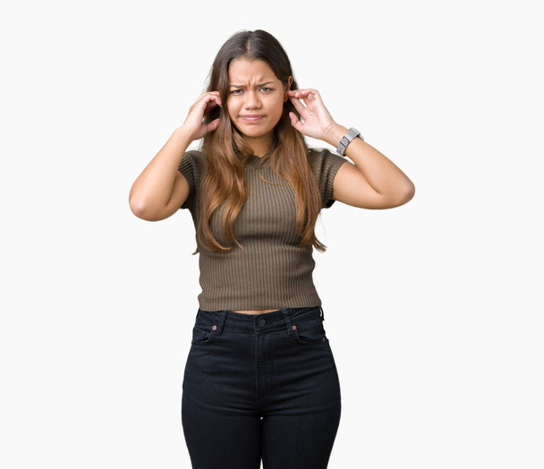 Young beautiful brunette woman over isolated background covering ears with fingers with annoyed expression for the noise of loud music. Deaf concept. - Foto, Imagen