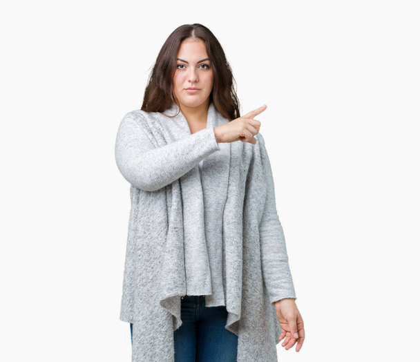 Beautiful plus size young woman wearing winter jacket over isolated background Pointing with hand finger to the side showing advertisement, serious and calm face - Valokuva, kuva