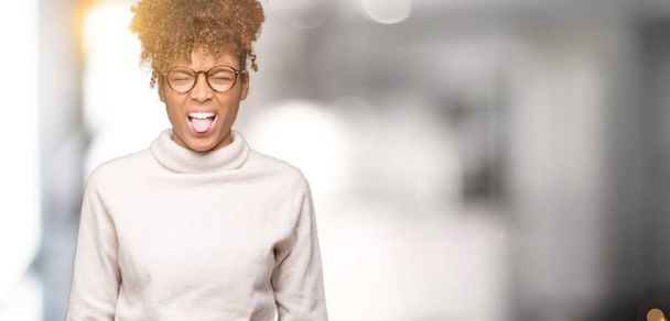 Όμορφη νεαρή αφρικανική αμερικανική γυναίκα φοράει γυαλιά πέρα από το απομονωμένο υπόβαθρο να κολλήσει τη γλώσσα έξω χαρούμενος με αστεία έκφραση. Αντίληψη των συναισθημάτων. - Φωτογραφία, εικόνα