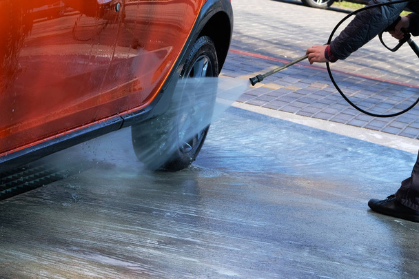Mosás tiszta vízzel önkiszolgáló autómosó. Az ember mossa a narancssárga autót autómosó a szabadban. - Fotó, kép