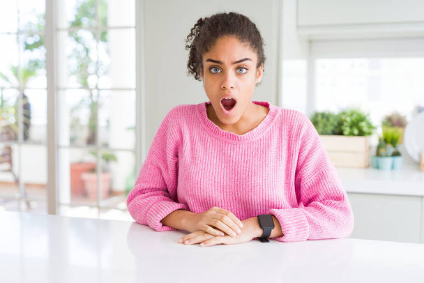 Beautiful african american woman with afro hair wearing casual pink sweater In shock face, looking skeptical and sarcastic, surprised with open mouth - Photo, Image