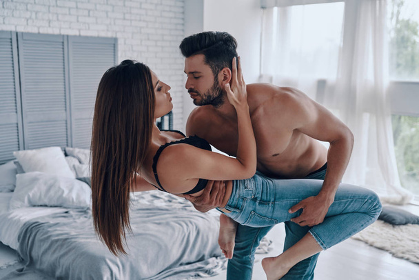 Beautiful young couple embracing in bedroom, man holding and carrying woman  - Fotoğraf, Görsel