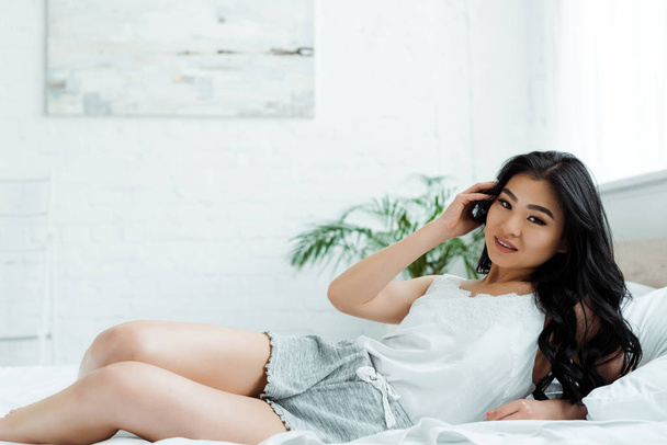 happy asian girl lying on bed and touching hair  - Valokuva, kuva