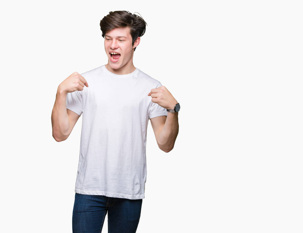 junger gutaussehender Mann, der legeres weißes T-Shirt über isoliertem Hintergrund trägt, sieht selbstbewusst aus, mit einem Lächeln im Gesicht, und zeigt mit den Fingern stolz und glücklich. - Foto, Bild