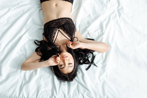 top view of thai woman with closed eyes in black sexy underwear lying on bed  - Φωτογραφία, εικόνα