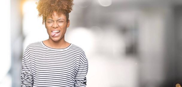 schöne junge afrikanisch-amerikanische Frau mit Brille über isoliertem Hintergrund streckt die Zunge glücklich mit lustigem Ausdruck heraus. Emotionales Konzept. - Foto, Bild