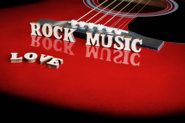 Slova Love Rock Music dřevěnými písmeny, na odrazném povrchu akustické kytary. Pohled na kytarový most. Tvůrčí pozadí. - Fotografie, Obrázek