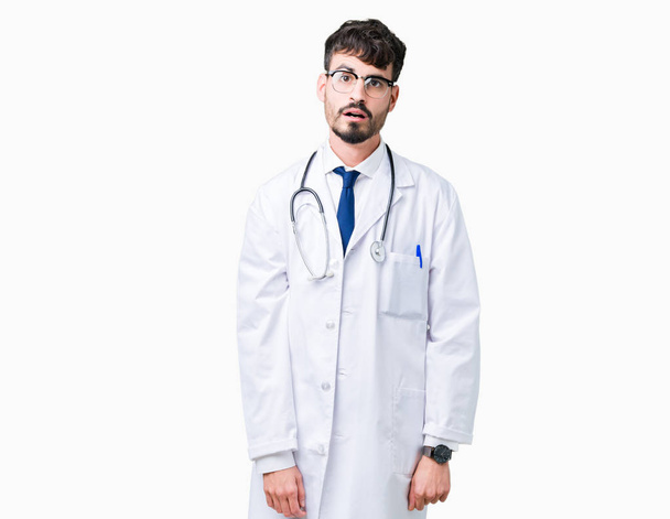Молодой врач в больничном пальто на изолированном фоне, напуганный и шокированный удивлением выражения лица, страха и возбужденного лица
. - Фото, изображение