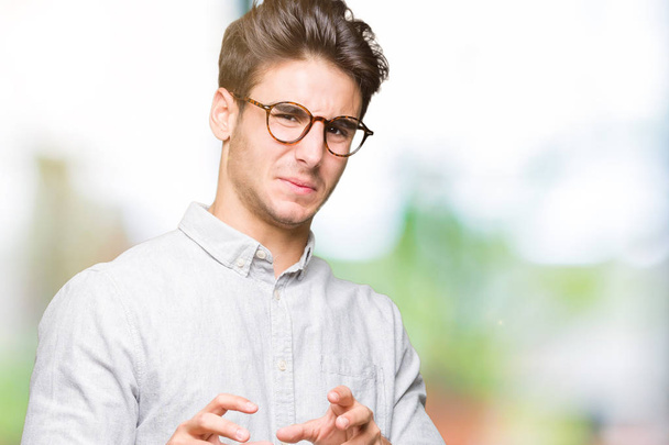 Young handsome man wearing glasses over isolated background disgusted expression, displeased and fearful doing disgust face because aversion reaction. With hands raised. Annoying concept. - Photo, Image