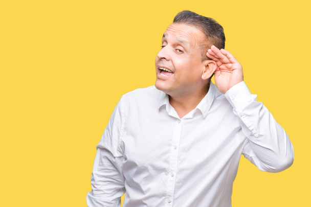 Арабський елегантний чоловік середнього віку над ізольованим тлом, посміхаючись рукою над вухом, слухаючи чутки або плітки. Концепція глухоти
. - Фото, зображення
