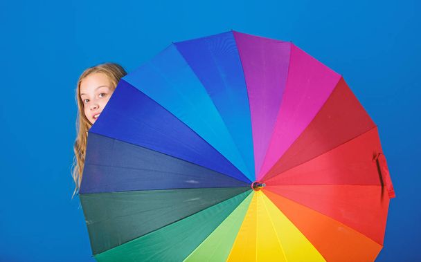 Weather forecast concept. Stay positive though rainy day. Brighten up life. Kid peek out colorful rainbow umbrella. Color your life. Girl cheerful hide behind umbrella. Colorful umbrella accessory - Фото, зображення