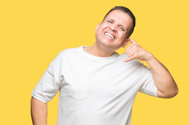Moyen Age arabe homme wearig t-shirt blanc sur fond isolé souriant faire geste de téléphone avec la main et les doigts comme parler au téléphone. Communication des concepts
. - Photo, image