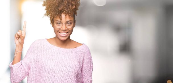 Güzel genç Afrikalı-Amerikalı kadın ve kendinden emin ve mutlu gülümseyerek süre parmak numaralı yukarıyı gösteren izole arka plan üzerinde gözlük. - Fotoğraf, Görsel