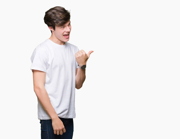Jonge knappe man dragen casual wit t-shirt over geïsoleerde achtergrond glimlachend met blij gezicht kijken en naar de kant met duim omhoog. - Foto, afbeelding