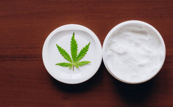 Crema hidratante para manos de cáñamo en dosis con hoja de cannabis verde. C
 - Foto, imagen