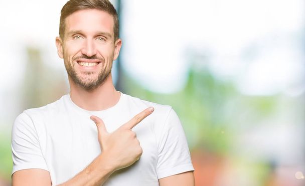 Hombre guapo vistiendo casual camiseta blanca alegre con una sonrisa de la cara señalando con la mano y el dedo hacia arriba a un lado con expresión feliz y natural en la cara
 - Foto, imagen