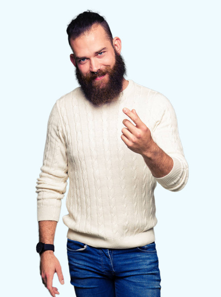 Young hipster man wearing winter sweater Beckoning come here gesture with hand inviting happy and smiling - Foto, Imagen