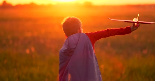 Jonge jongen piloot en loopt in het veld bij zonsondergang en spelen met vliegtuig dromen - Video