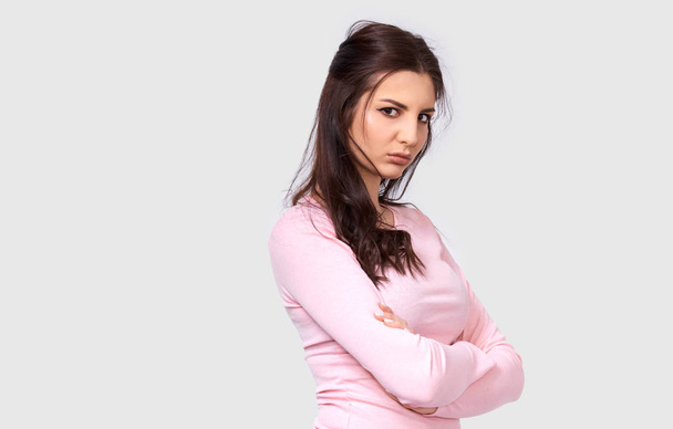 Vnitřní záběr smutné mladé bruneté ženy má unavené obličeje, nosí růžovou halenku, která se drží za ruce, izolovaná na bílém pozadí. Střela z pěkně rozčilená žena přes šedou zeď studia - Fotografie, Obrázek