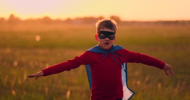 Junge in Superheldenkostüm und Maske läuft bei Sonnenuntergang träumend und fantasierend über das Feld - Filmmaterial, Video