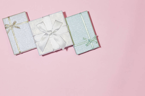 Festive background with gift wrapping with an assortment of boxes of pink, silver, pale blue, color with a bow in pastel colors on a delicate pink background with a copy space - 写真・画像