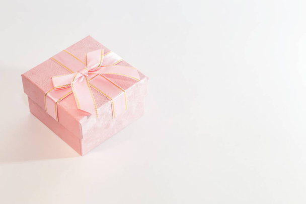 Festive background with gift wrap with a box of pink color with a bow in pastel colors on a white background with copy space - Photo, image