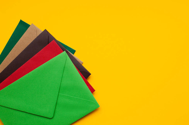 黄色の背景に赤、茶色、緑の封筒、テキスト用のスペース、トップビュー - 写真・画像