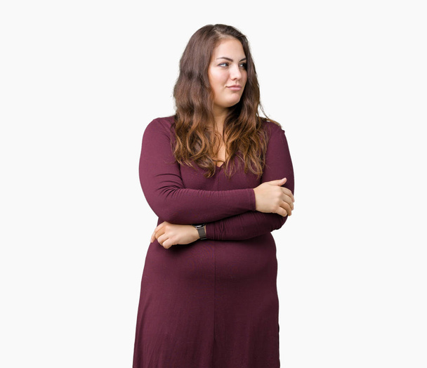 Mooi en aantrekkelijk plus grootte jonge vrouw draagt een jurk op geïsoleerde achtergrond glimlachend op zoek naar de kant met gekruiste armen ervan overtuigd en vertrouwen - Foto, afbeelding