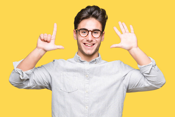 Όμορφος νεαρός φορώντας γυαλιά πάνω από απομονωμένες φόντο και στραμμένο προς τα επάνω με τα δάχτυλά σας αριθμός επτά ενώ χαμογελώντας αυτοπεποίθηση και χαρούμενοι. - Φωτογραφία, εικόνα