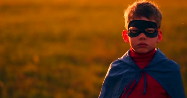 Το αγόρι με τη μάσκα και το ακρωτήριο ενός σούπερ ήρωα στο ηλιοβασίλεμα σε ένα χωράφι - Πλάνα, βίντεο