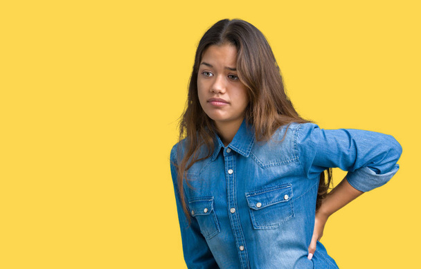 Young beautiful brunette woman wearing blue denim shirt over isolated background Suffering of backache, touching back with hand, muscular pain - Photo, Image