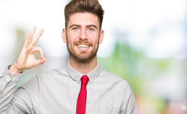Young handsome business man smiling positive doing ok sign with hand and fingers. Successful expression. - Photo, Image