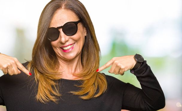 Beautiful middle age woman wearing sunglasses looking confident with smile on face, pointing oneself with fingers proud and happy. - Fotografie, Obrázek