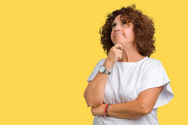 Beautiful middle ager senior woman wearing white t-shirt over isolated background with hand on chin thinking about question, pensive expression. Smiling with thoughtful face. Doubt concept. - Photo, Image