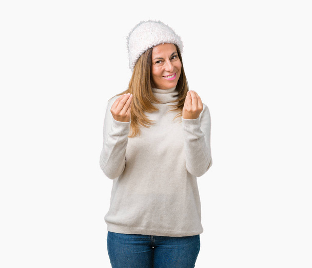 Mooie middelbare leeftijd vrouw winter trui en muts dragen over geïsoleerd achtergrond doen geld gebaar met hand, vraagt om salarisbetaling, miljonair business - Foto, afbeelding