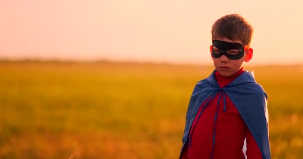 Portrét chlapce v masce super hrdiny, jak se dívá na kameru stojící v poli při západu slunce. - Záběry, video