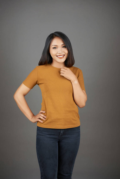 Portrait of pretty young Vietnamese woman in bright orange top posing against grey background - Foto, Imagem