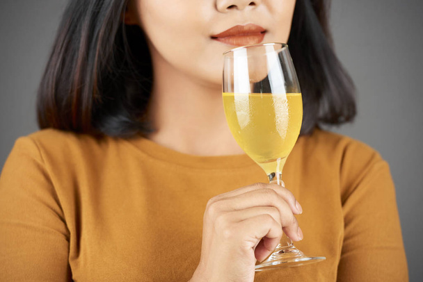 Молодая женщина, поддерживающая вкусный запах свежего фруктового сока в бокале вина
 - Фото, изображение