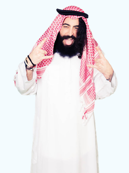 アラビア ビジネス伝統的なクーフィーヤ スカーフを手でロックのシンボルをやってクレイジー式で叫びを身に着けている長い髪の男。音楽の星。重いコンセプト. - 写真・画像