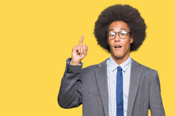 Jovem homem de negócios afro-americano com cabelo afro usando óculos apontando dedo para cima com ideia de sucesso. Saído e feliz. Número um.
. - Foto, Imagem