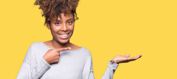 Gyönyörű fiatal afrikai-amerikai nő több mint meghökkent, és mosolyog a kamerába, miközben bemutatja a kezét és ujjával mutatva elszigetelt háttér. - Fotó, kép