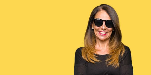 Beautiful middle age woman wearing sunglasses happy face smiling with crossed arms looking at the camera. Positive person. - Photo, Image