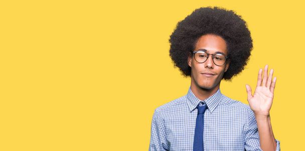 junger afrikanisch-amerikanischer Geschäftsmann mit Afro-Haaren und Brille, der darauf verzichtet, fröhlich und lächelnd Hallo zu sagen, freundliche Willkommensgeste - Foto, Bild