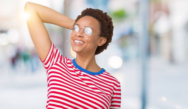 Piękna młoda kobieta Afroamerykanów w okularach na białym tle uśmiechający się pewnie włosy dotykając ręką się gest, pozowanie atrakcyjne - Zdjęcie, obraz