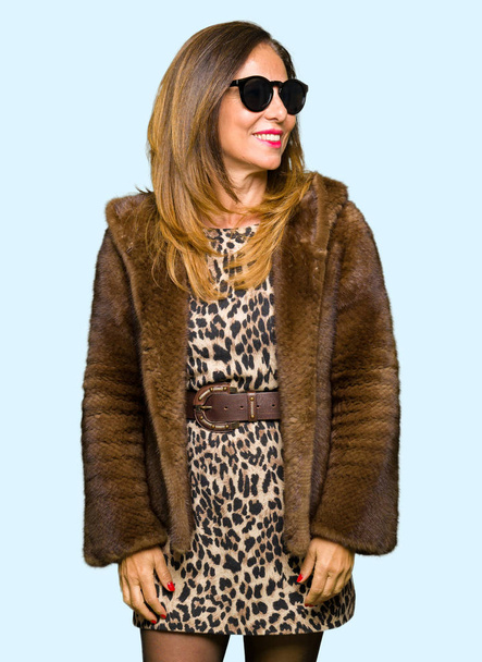 Beautiful middle age elegant woman wearing sunglasses and mink coat looking away to side with smile on face, natural expression. Laughing confident. - Фото, зображення